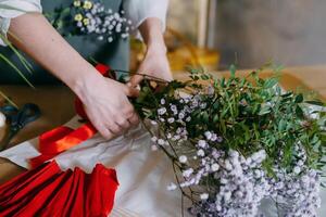 florist works on preparing beautiful floral arrangement. Various flowers and materials lie on table, emphasizing artistic and inspiring atmosphere associated with floral design and presentation. photo