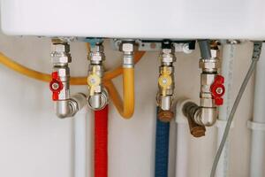 Close-up view of water heater pipes and valves in a utility room, featuring colorful connectors and tubes. Essential components for heating system maintenance and operation. Gas boiler taps. photo