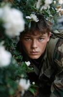 Teenage boy in camouflage hiding behind white flowers photo