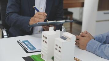 A real estate agent is writing on a clipboard while a man is looking at a model of a video