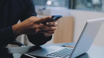 A man using his phone while sitting at a desk with a laptop video