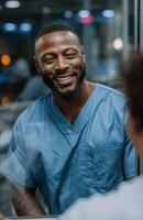 Smiling doctor wearing blue scrubs talking to patient behind glass in hospital photo