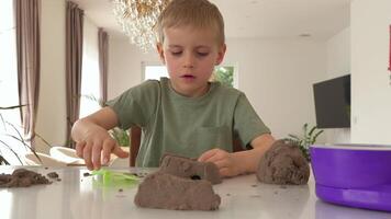 A boy enjoys hands-on play with sand, forming shapes and patterns on a glass table. His concentrated expression reflects deep engagement in this tactile and artistic activity video
