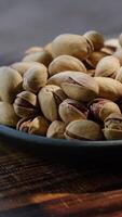 Vertical nuts background. Roasted pistachios nuts in bowl on wooden table. video
