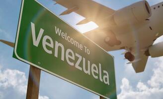 Welcome To Venezuela Green Road Sign with Low Flying Airplane Just Above with Landing Gear Down. photo