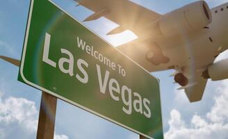 Welcome To Las Vegas Green Road Sign with Low Flying Airplane Just Above with Landing Gear Down. photo