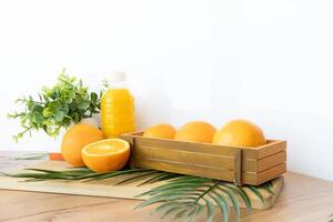 Fresh oranges and juice bottle on wood table with green plant and palm leaf in front of yellow backdrop Flatlay with oranges and juice bottle on wooden surface and white background with tropical palm photo