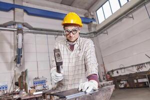 a blacksmith in work clothes with helmet and protective glasses working with hammer and anvil photo