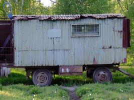 Old mobile shed resting on wheels in a green field surrounded by trees photo