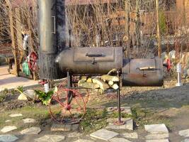 Old smoker grill placed in a backyard garden surrounded by wood piles photo