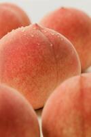 Extreme close-up of a ripe peach covered in fresh water droplets, surrounded by other peaches softly blurred in the foreground and background photo