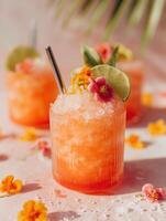Refreshing summer cocktail in orange-pink tone with crushed ice, lime slice, edible flowers, and a metal straw in a ribbed glass. photo