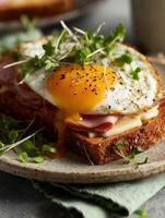 Realistic food photography in film style whole grain toast topped with slices of ham, melted cheese, and a fried egg with bright runny yolk sprinkled with black pepper. photo