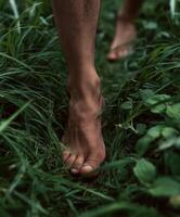 A close-up photo of bare feet walking slowly through dense, lush green grass, toes sinking gently into the soft blades.