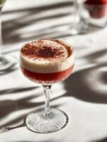 Elegant cocktail in a vintage-stemmed glass, featuring two layers a deep ruby-red bottom and a creamy frothy top, dusted with cocoa powder. photo
