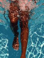 A hyper-realistic underwater close-up of a womans legs and feet as she swims in a clear blue swimming pool. photo