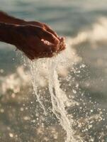 A close-up shot of adult hands gently cupping and lifting water from the sea, with clear splashes and shimmering droplets illuminated by golden sunlight. photo