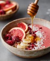 A delicious pink smoothie bowl topped with grapefruit slices, banana, raspberries, shredded coconut, and pomegranate seeds. photo