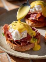 Realistic food photography in film style toast with prosciutto, leafy greens, and poached egg, topped with thick hollandaise sauce being drizzled from a spoon. photo