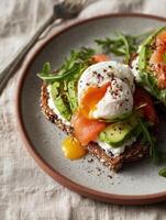 Realistic photo in minimal natural light style of seeded whole grain toast topped with whipped cream cheese, fresh avocado slices, smoked salmon, and a perfectly poached egg with a runny yolk