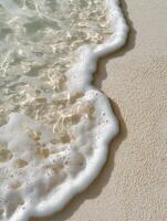 A minimalistic top-down view of soft sea foam gently touching the fine sand on a tropical beach. photo