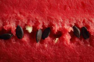 Macro photograph of ripe red watermelon pulp with a vertical line of black seeds centered in the frame. photo