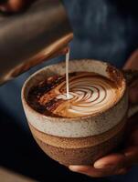 Macro close-up of milk being poured into a latte with cocoa powder and swirled latte art, captured in a handmade ceramic cup. photo