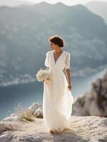 Full-length portrait of a bride standing on a mountain cliff in soft morning or evening sunlight. photo