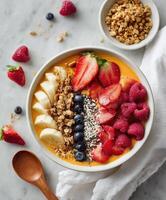 A vibrant smoothie bowl with a mango base, topped with fresh strawberries, raspberries, blueberries, banana slices with chia seeds, and sprinkled granola. photo