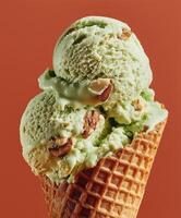 Close-up of a waffle cone holding three scoops of green ice cream with visible crumbs, set against a plain terracotta background. photo