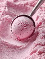 Close-up of a metal ice cream scoop lifting a ball of soft pink ice cream with a creamy texture and light speckles. photo