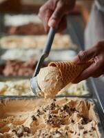 Lifestyle food photo close-up of hands scooping caramel gelato with a metal spatula and placing it into a waffle cone.