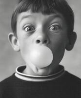 A freckled boy with messy hair blows a pink bubble gum bubble making a silly and mischievous expression. photo