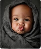 A close-up portrait of an adorable baby wrapped snugly in a dark gray linen blanket, making a funny kissy face with puckered lips. photo