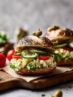 Realistic food photography of a gourmet sandwich with poppy seed bun, creamy egg salad, fresh lettuce, tomato slices, and cucumber pickles, topped with a mini pickled gherkin on a wooden board. photo
