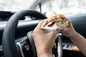 lady holding hamburger to eat in car, dangerous photo