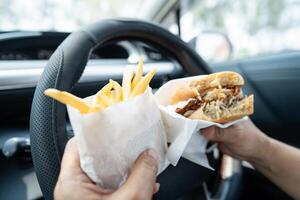lady holding hamburger to eat in car, dangerous and risk an accident. photo