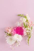 A round bottle of pink perfume on a pink background with fresh flowers. vertical top view. An empty mockup of a non-branded bottle. A copy space photo
