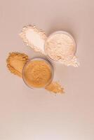 Two cosmetic glass jars with dry loose powder in natural and bronze tones stand on the powder texture samples. vertical top view. A copy space. photo