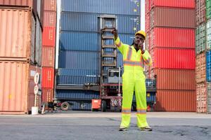 Foreman dock worker in hardhat and safety vest talks on two-way radio control loading containers box from container cargo photo