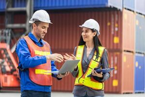 Female foreman in safety vest using clipboard checklist and Engineer man in hardhat holding laptop for control loading containers box from cargo photo