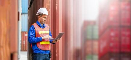 Engineer man with laptop checking containers box in in industry containers yard, Foreman dock worker inspecting containers box photo