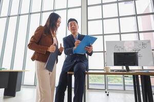 Asian businesspeople meeting in office, Two business professionals discussing documents in modern office, Team meeting and brainstorming concepts photo