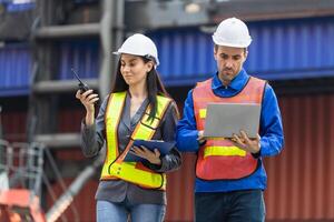 Female foreman safety vest using clipboard checklist and Engineer man in hardhat holding laptop for control loading containers box from cargo photo