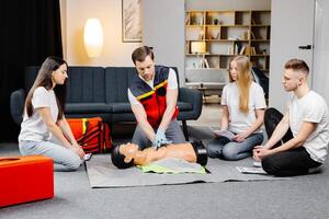 Man instructor helping to make first aid heart compressions with dummy during the group training indoors photo