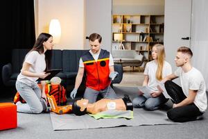 Young man instructor helping to make first aid heart compressions with dummy during the group training photo