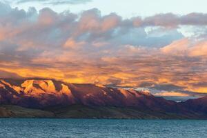 Gazing at the high-altitude lake Manasarovar at sunset in Tibet is a stunning experience. The sun's rays pierce through the clouds, casting a warm glow on the serene and smooth surface of the lake. photo