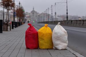 Garbage bags in red, yellow, and white placed on a city street at dawn photo