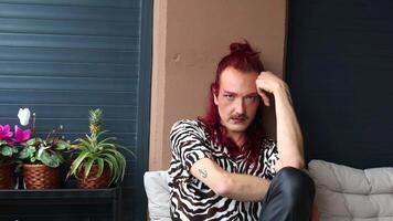Non-binary person with red hair and mustache posing on balcony video