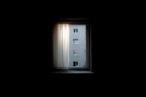 Light filters through a curtain, revealing a building across the street at dusk photo